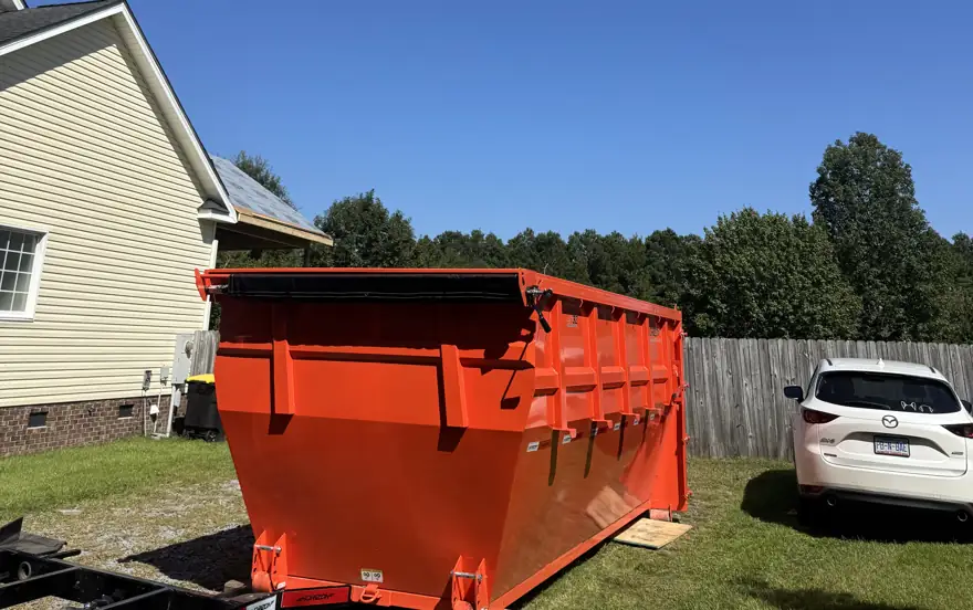 Orange roll-off dumpster freshly delivered to a yard